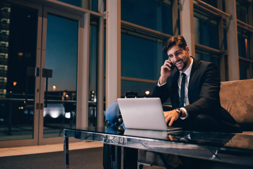 smiling_businessman_with_laptop_talking_on_cellphone_at_the_airport