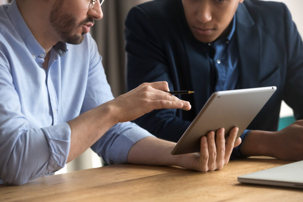 diverse_businessmen_talking_using_digital_tablet_sit_at_office_desk,