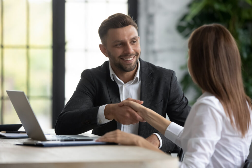 happy_businessman_shaking_hands_with_woman_job_seeker_near_laptop.